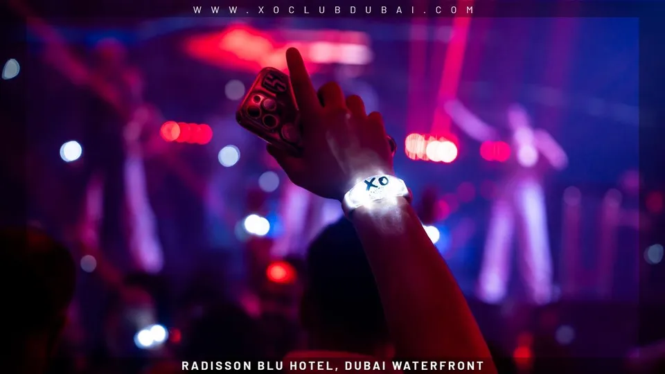 A raised hand wearing a glowing XO wristband on the dance floor at XO Club Dubai
